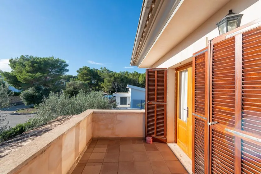 Un balcón embaldosado con contraventanas de madera da a árboles y edificios vecinos.