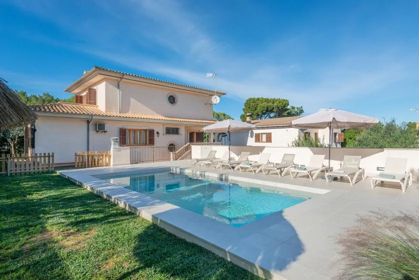 Piscina exterior junto a una casa, con asientos de descanso en el patio.