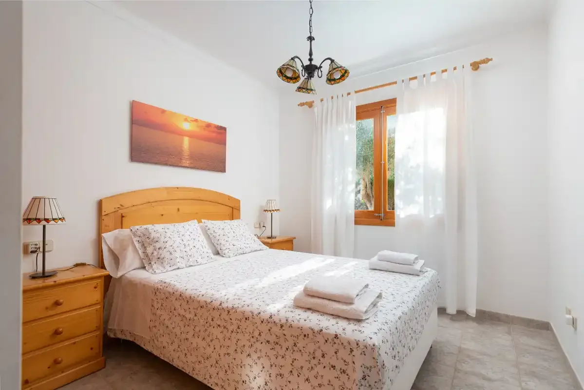 Un dormitorio con cama doble, mesitas de noche y una ventana con cortinas.