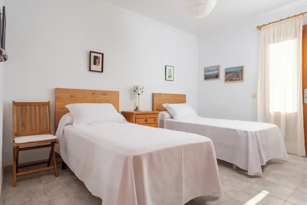 Un dormitorio con dos camas, cabeceros de madera y una ventana luminosa con cortinas.