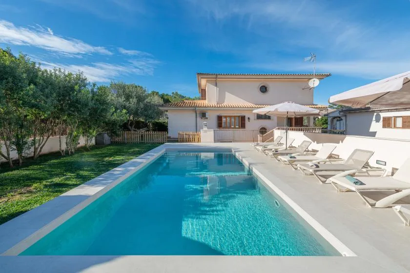 Outdoor swimming pool beside a house, with lounge seating along the deck.
