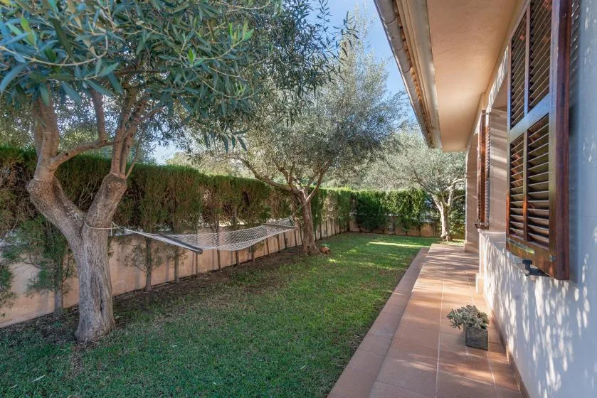 A garden beside a house, with a lawn, trees, and a paved walkway.