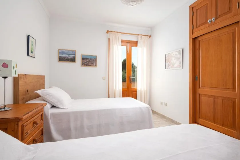 Un dormitorio luminoso con dos camas, muebles de madera y una puerta acristalada con cortinas.