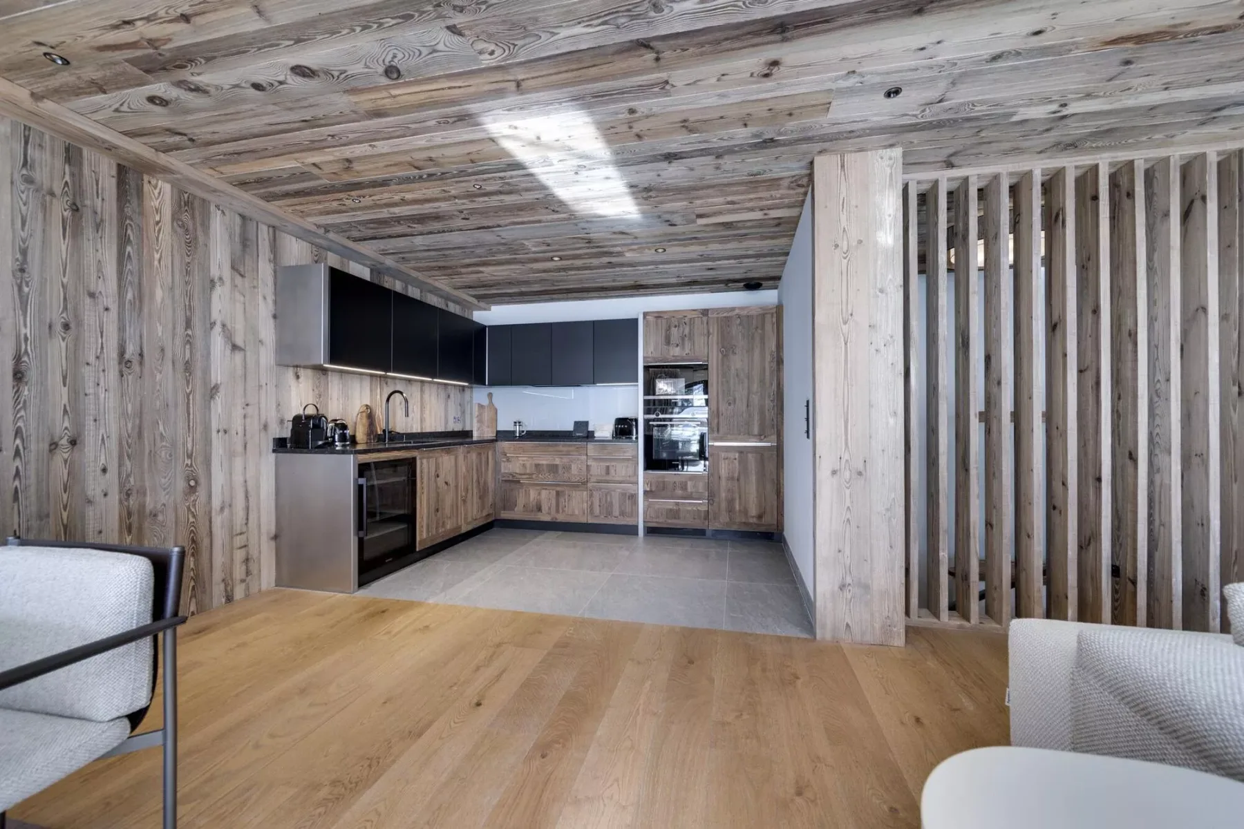 Una cocina con gabinetes de madera y piso de baldosas se abre a una zona de estar con piso de madera.