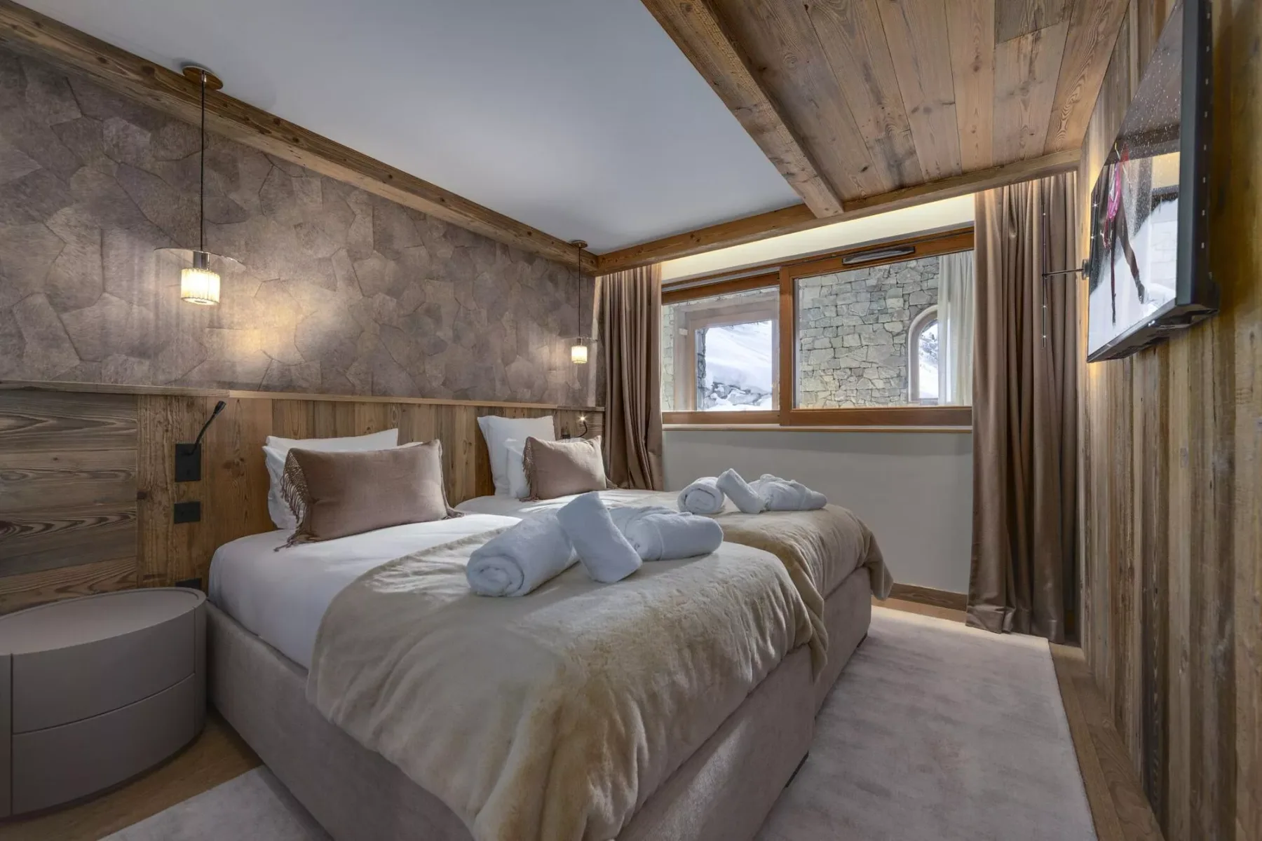 Dormitorio con dos camas, toallas dobladas y una ventana con vista a una pared de piedra.
