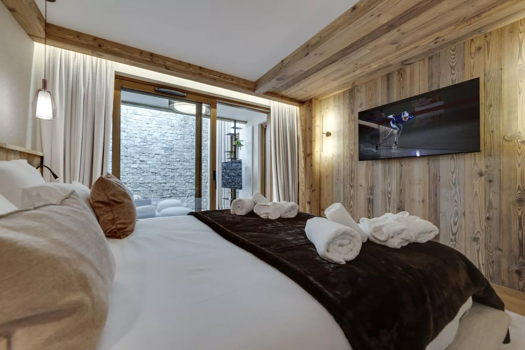 Un dormitorio con una cama, toallas dobladas y un televisor montado en la pared.