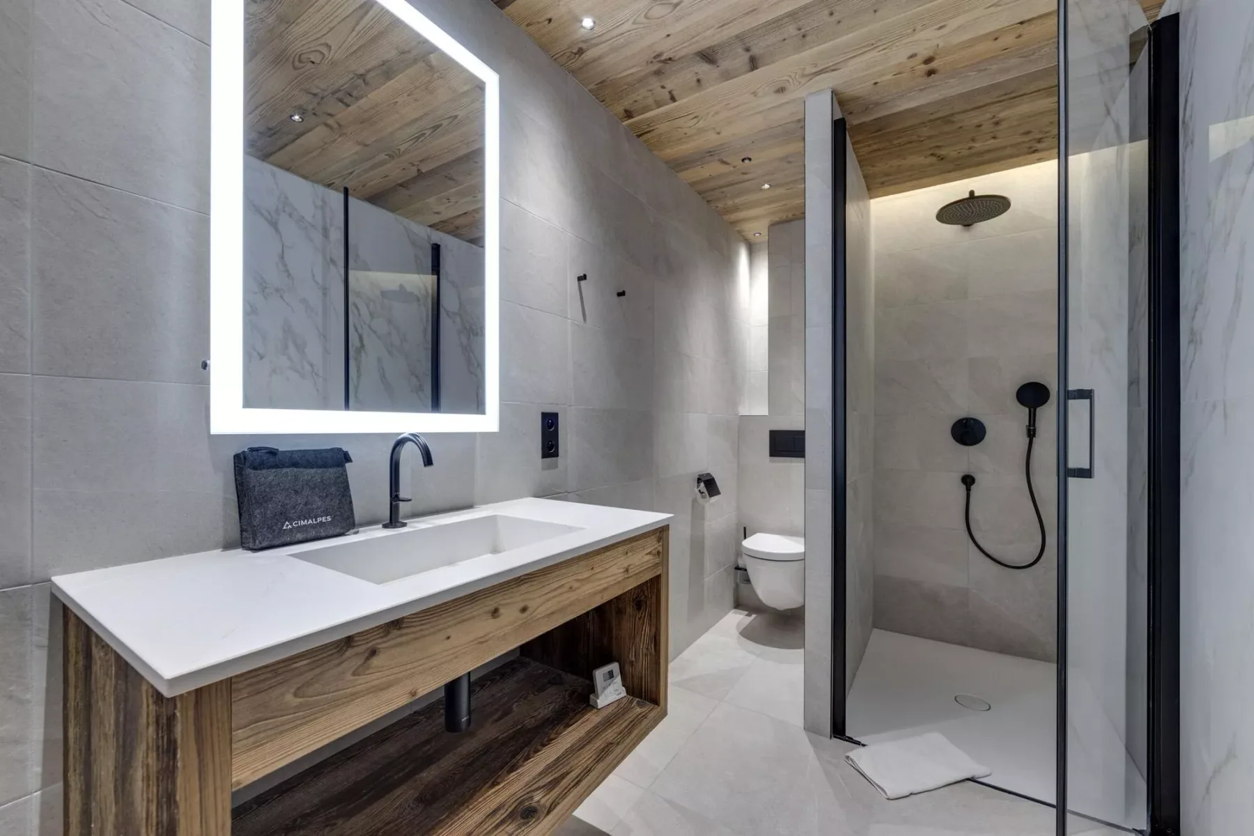 Un baño moderno con lavabo amplio, espejo iluminado, inodoro y ducha de vidrio.