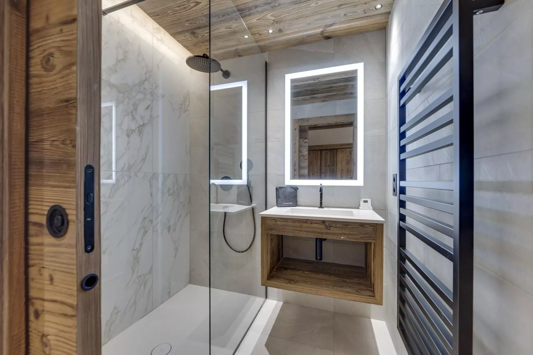 Un baño moderno con ducha de vidrio y un lavabo suspendido bajo un espejo iluminado.