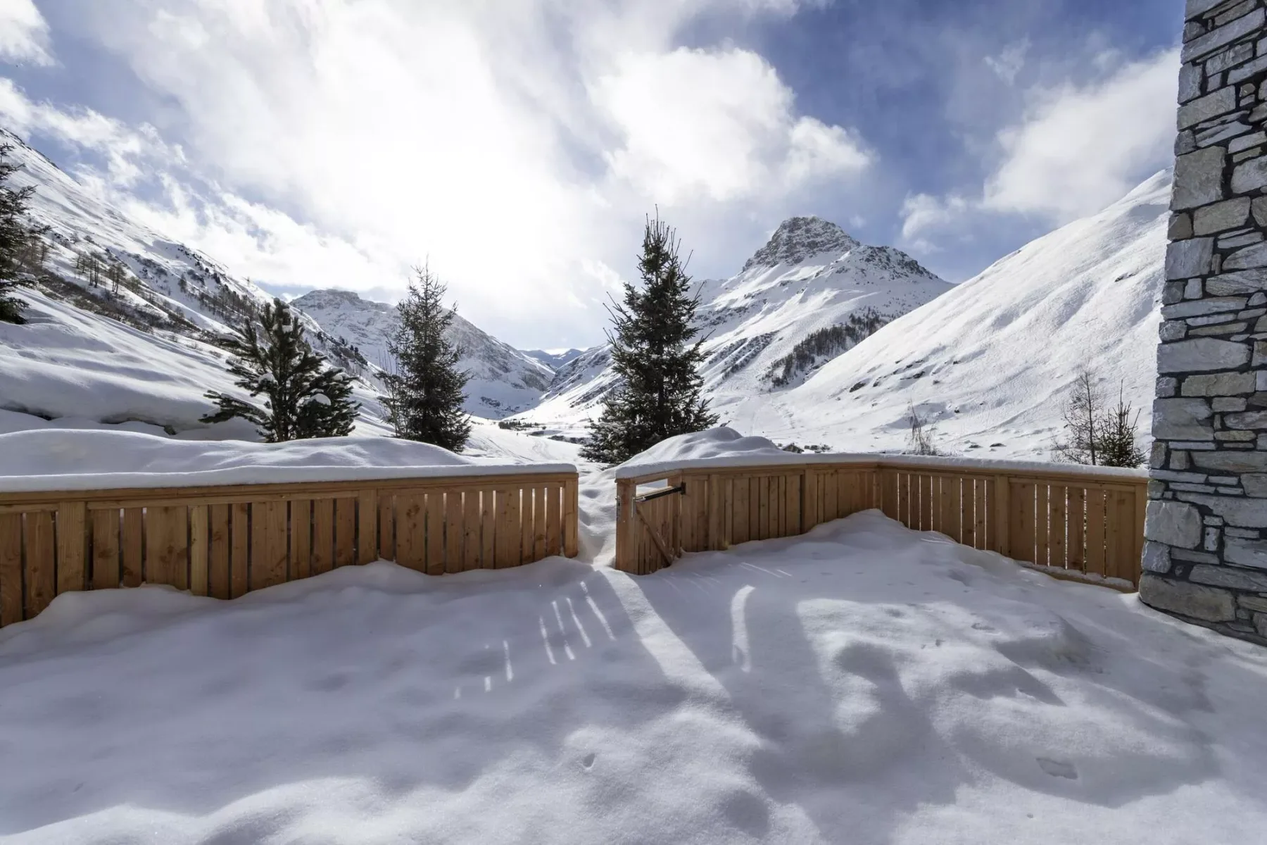 Una terraza cubierta de nieve da a un valle montañoso con árboles perennes.