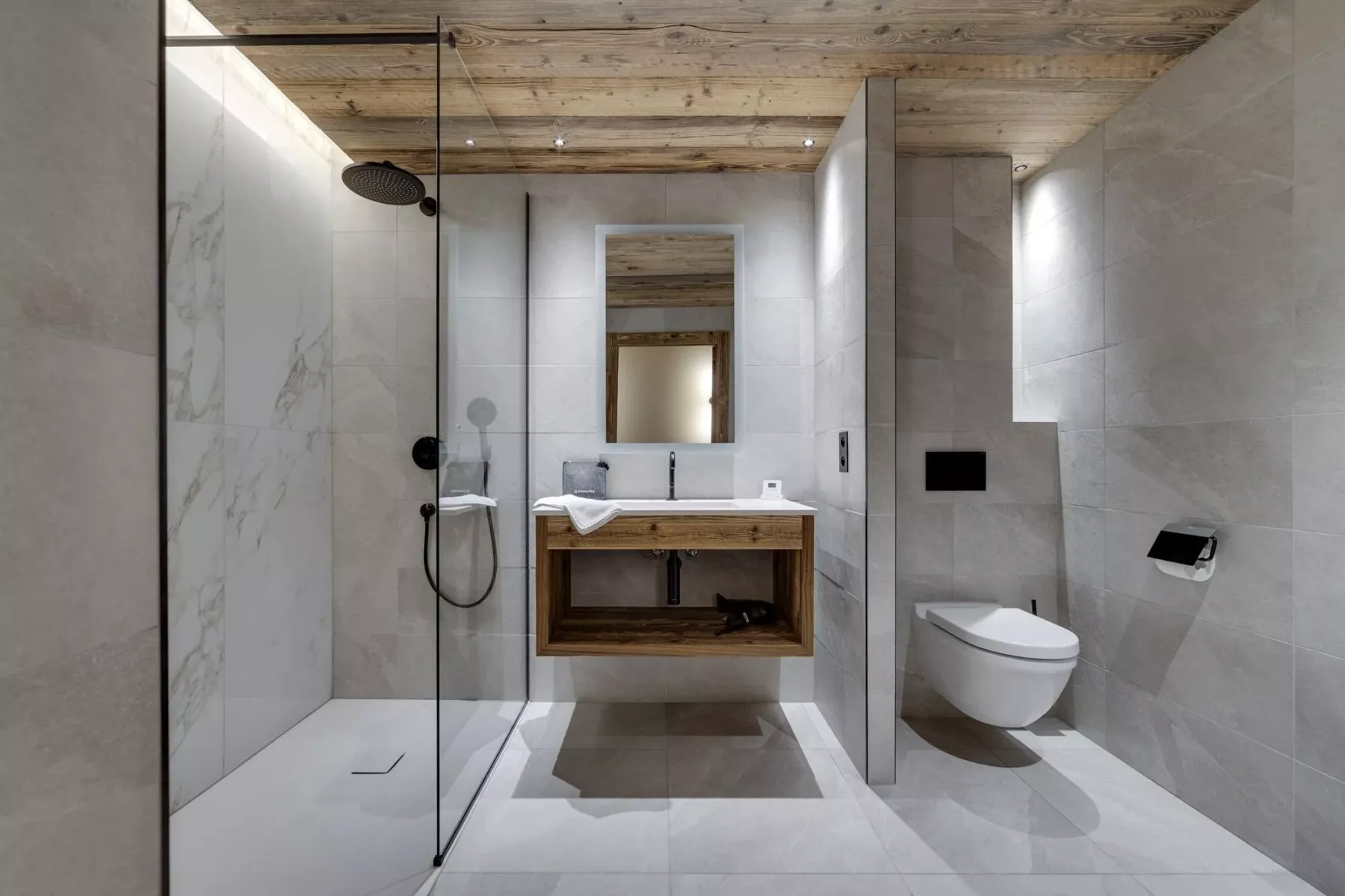 Un baño moderno con ducha de vidrio, inodoro suspendido y mueble de madera.