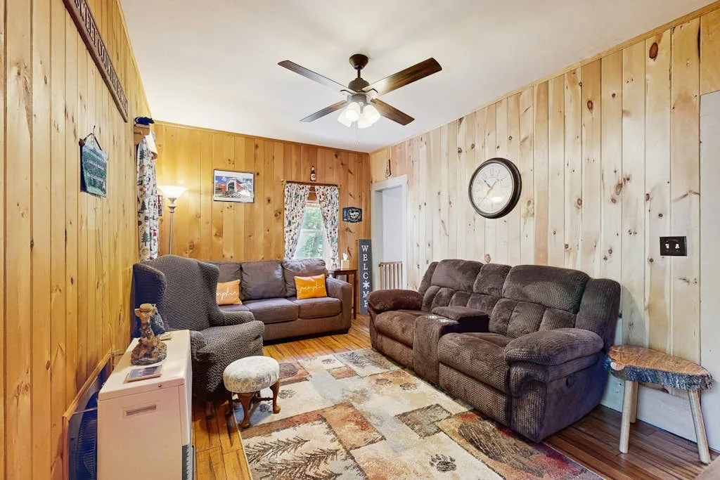 A wood-paneled living room with seating, a patterned rug, and a ceiling fan.