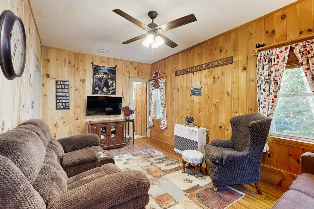 A wood-paneled living room with seating, a television, and a window.