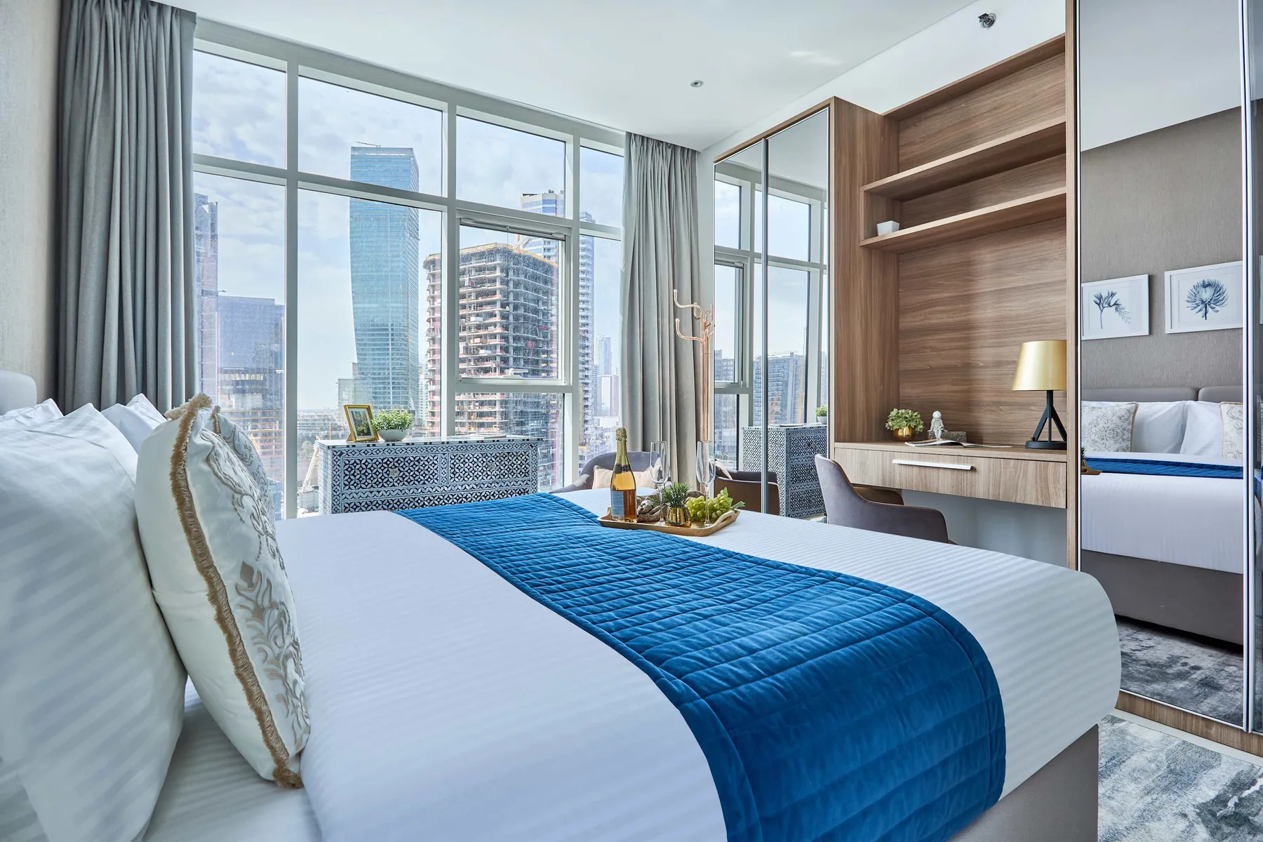 Un dormitorio con una cama bien tendida y ventanas de piso a techo con vistas a edificios.