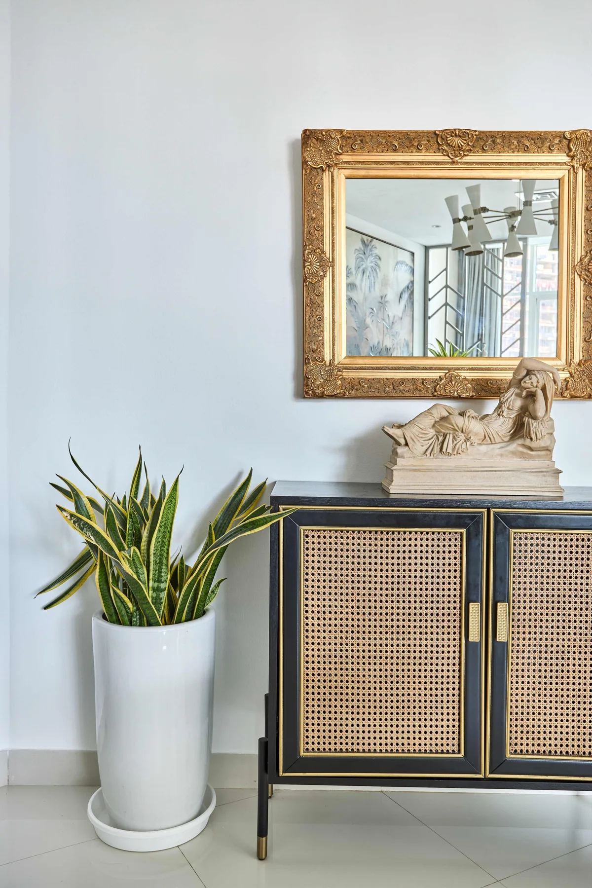 Un mueble decorativo con un espejo enmarcado y una planta en maceta está junto a una pared clara.