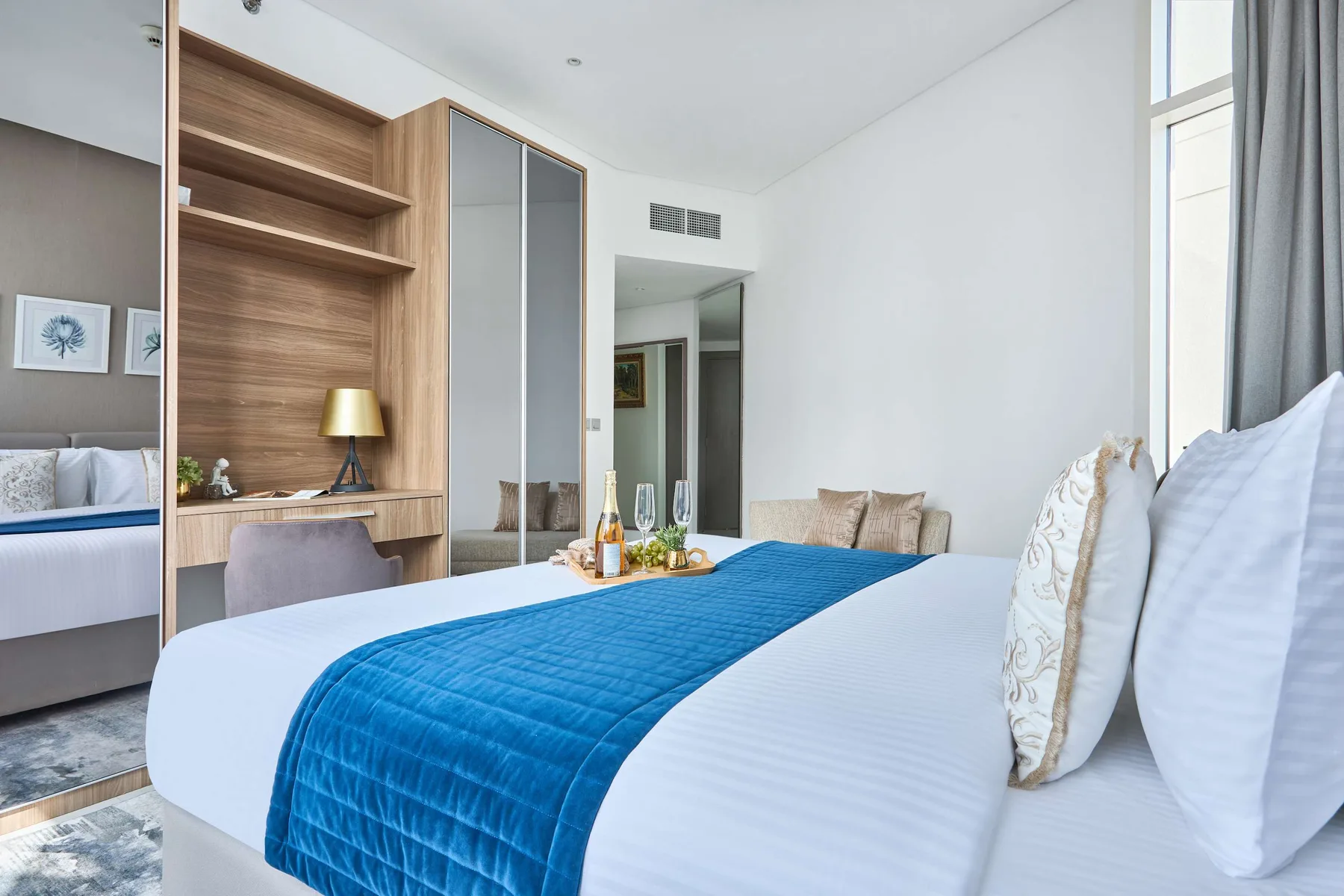 Un dormitorio luminoso con una cama tendida y una colcha azul junto a una ventana.