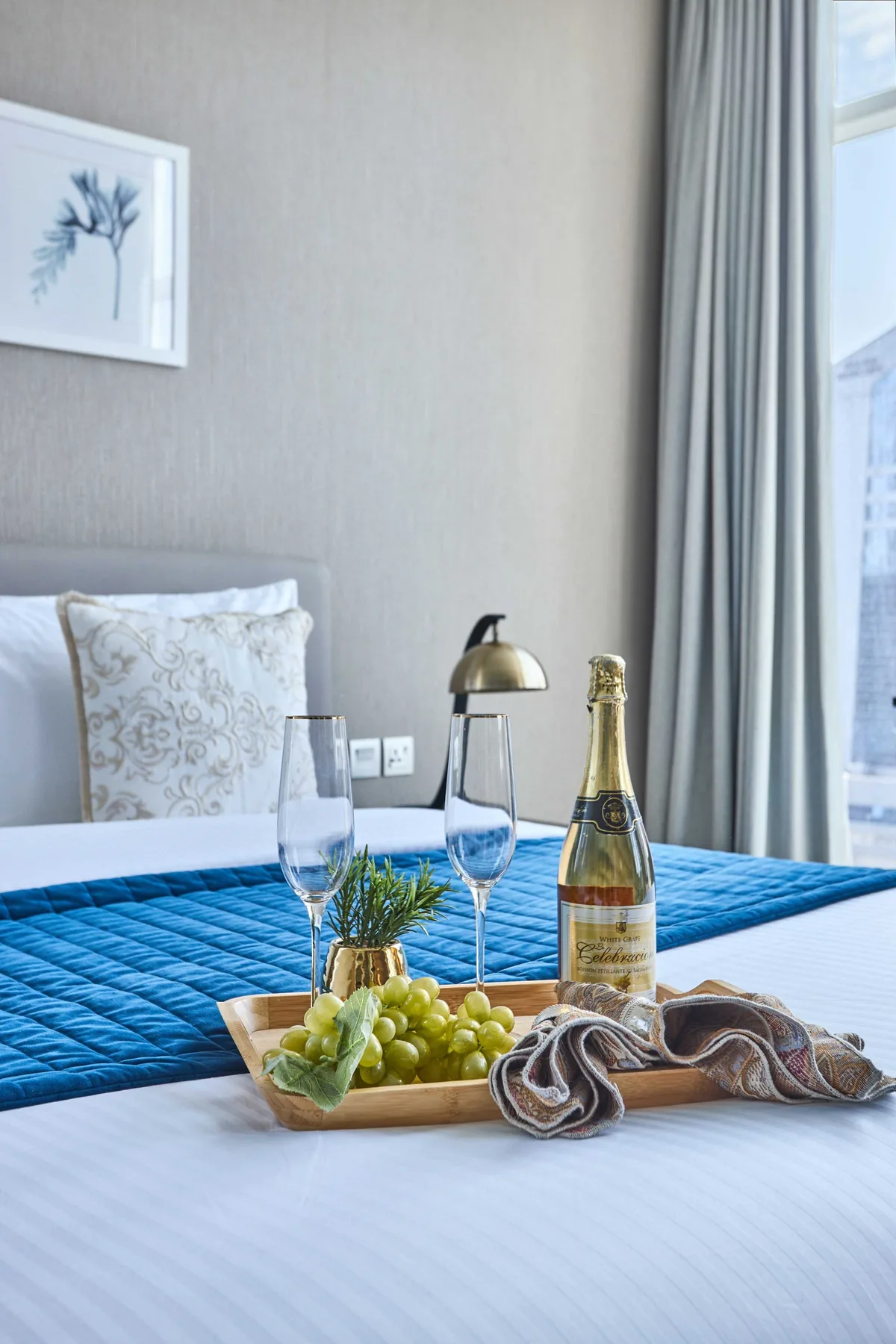 Un dormitorio con una cama bien arreglada y una bandeja con uvas y champán.