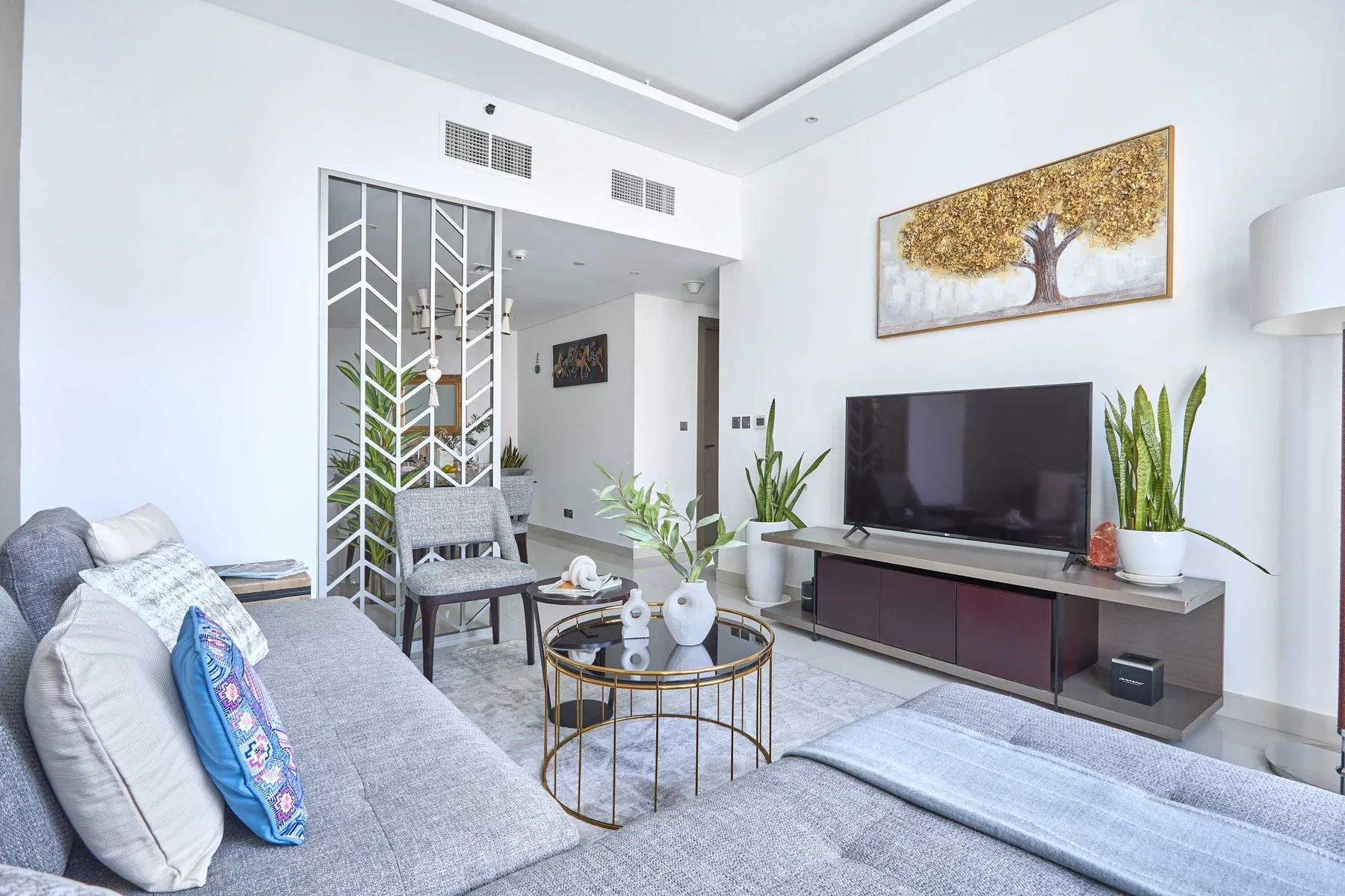 Una sala luminosa con asientos, un televisor, plantas y una mesa de centro redonda.