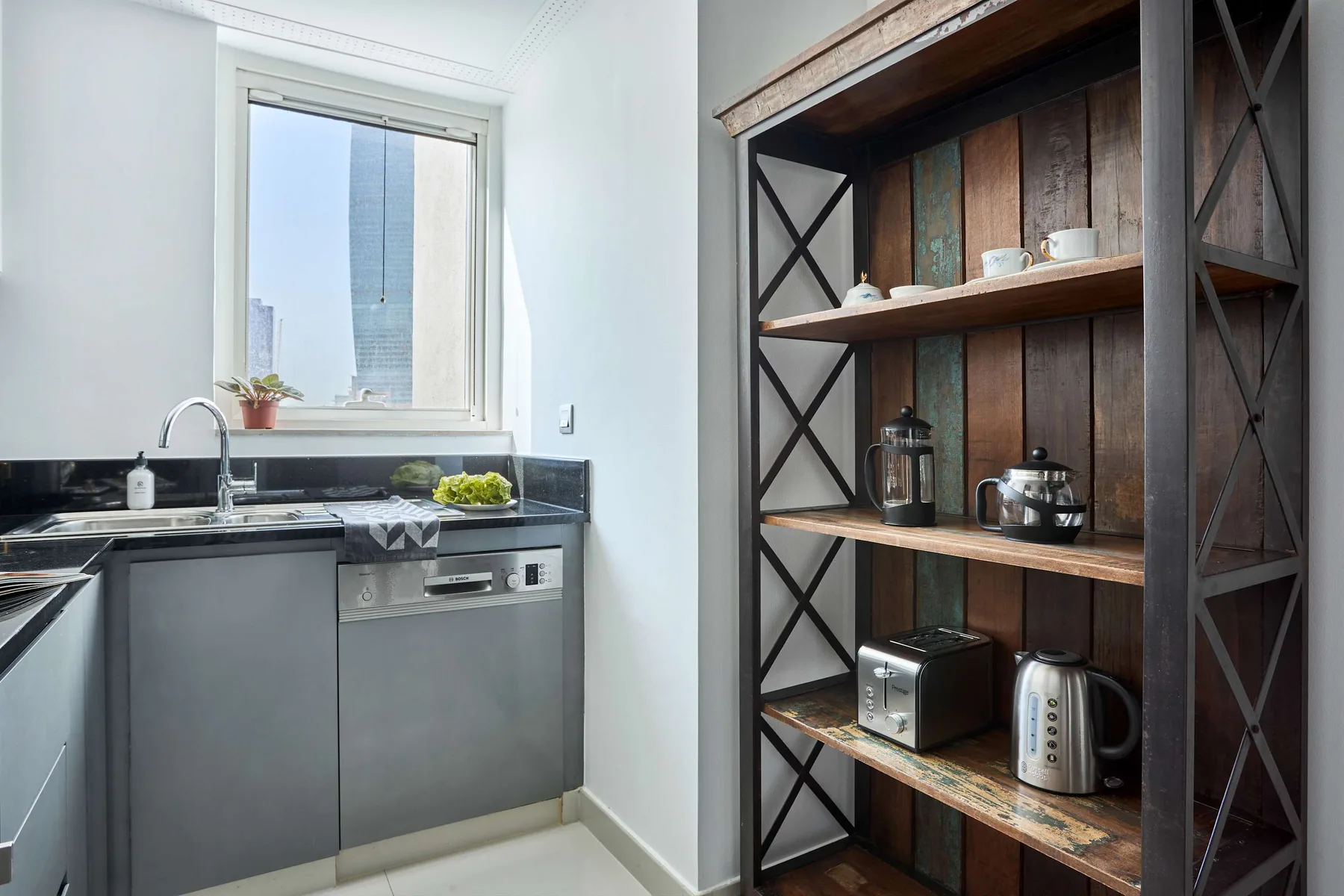 Una cocina compacta con fregadero, lavavajillas y estantes abiertos para pequeños electrodomésticos.