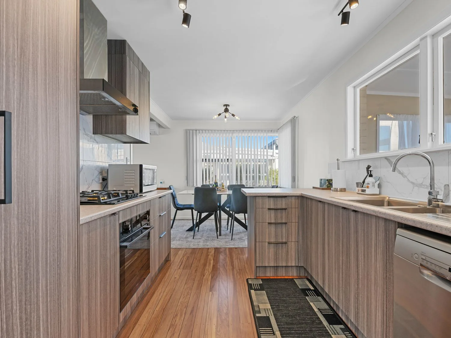 A kitchen with wooden cabinets, a gas stove, microwave, sink, dishwasher, and a dining area with a table and chairs at Owhata Retreat - Rotorua Holiday Home in Rotorua