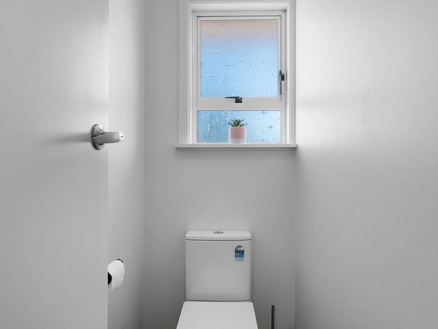 A small bathroom with a toilet under a window with frosted glass and a small plant on the windowsill at Owhata Retreat - Rotorua Holiday Home in Rotorua