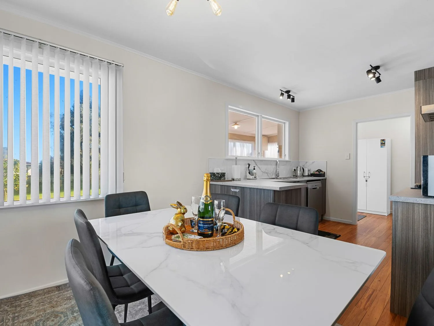 A dining area with black seating around a white table, with a kitchen in the background.