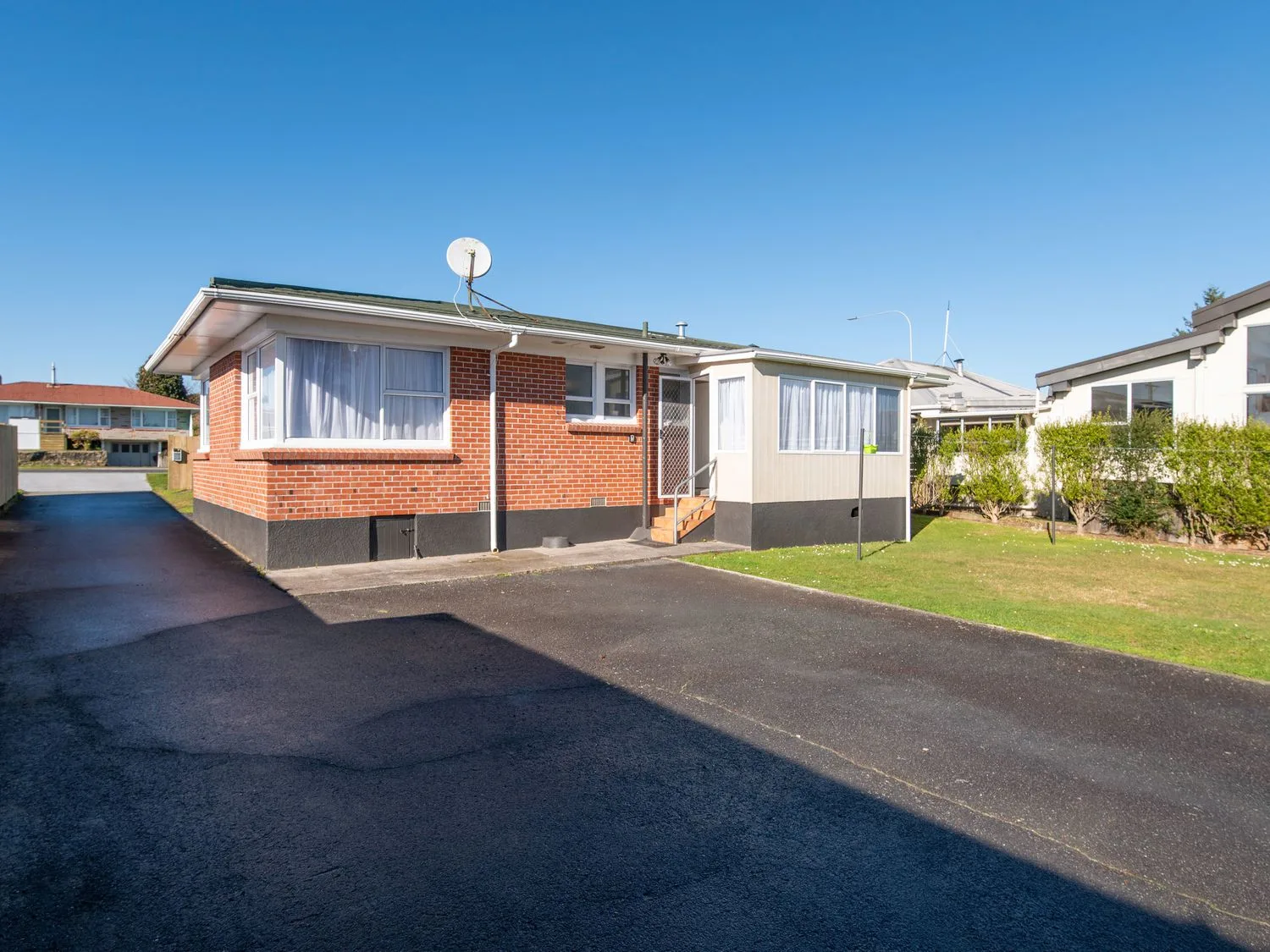 A single-story brick house with a tiled roof a driveway and a small lawn at Owhata Retreat - Rotorua Holiday Home in Rotorua