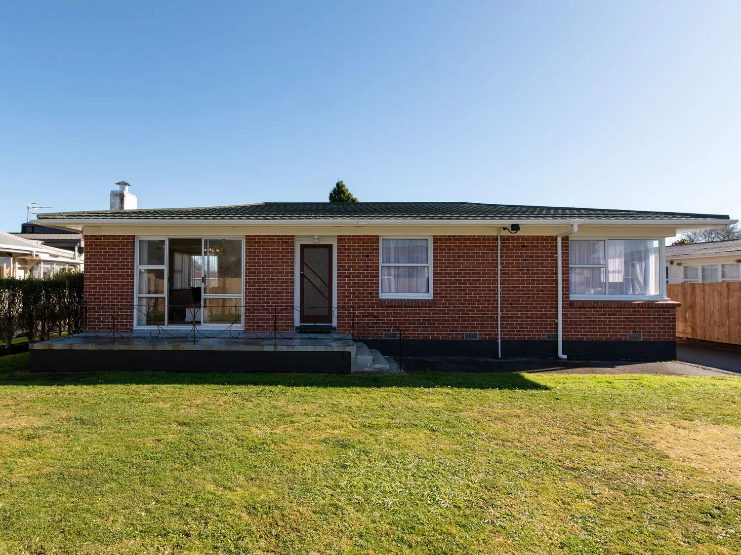 A single story brick house with a front door and windows and a grass lawn at Owhata Retreat - Rotorua Holiday Home in Rotorua