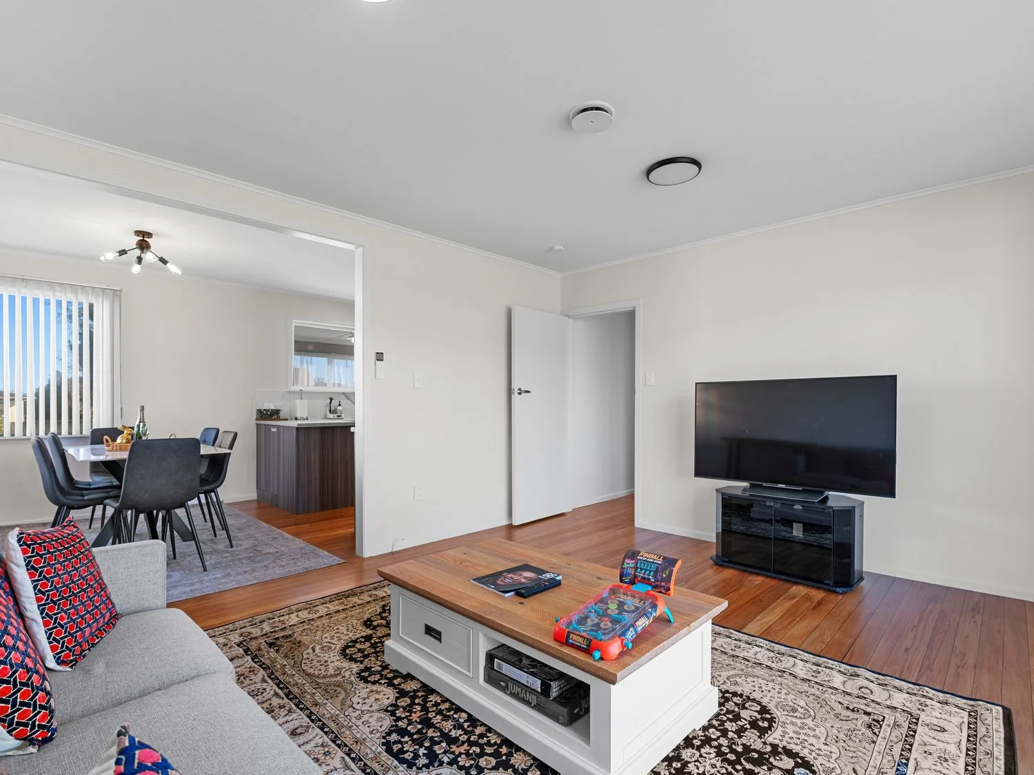 A living room with seating, a coffee table, and a television beside a dining area.
