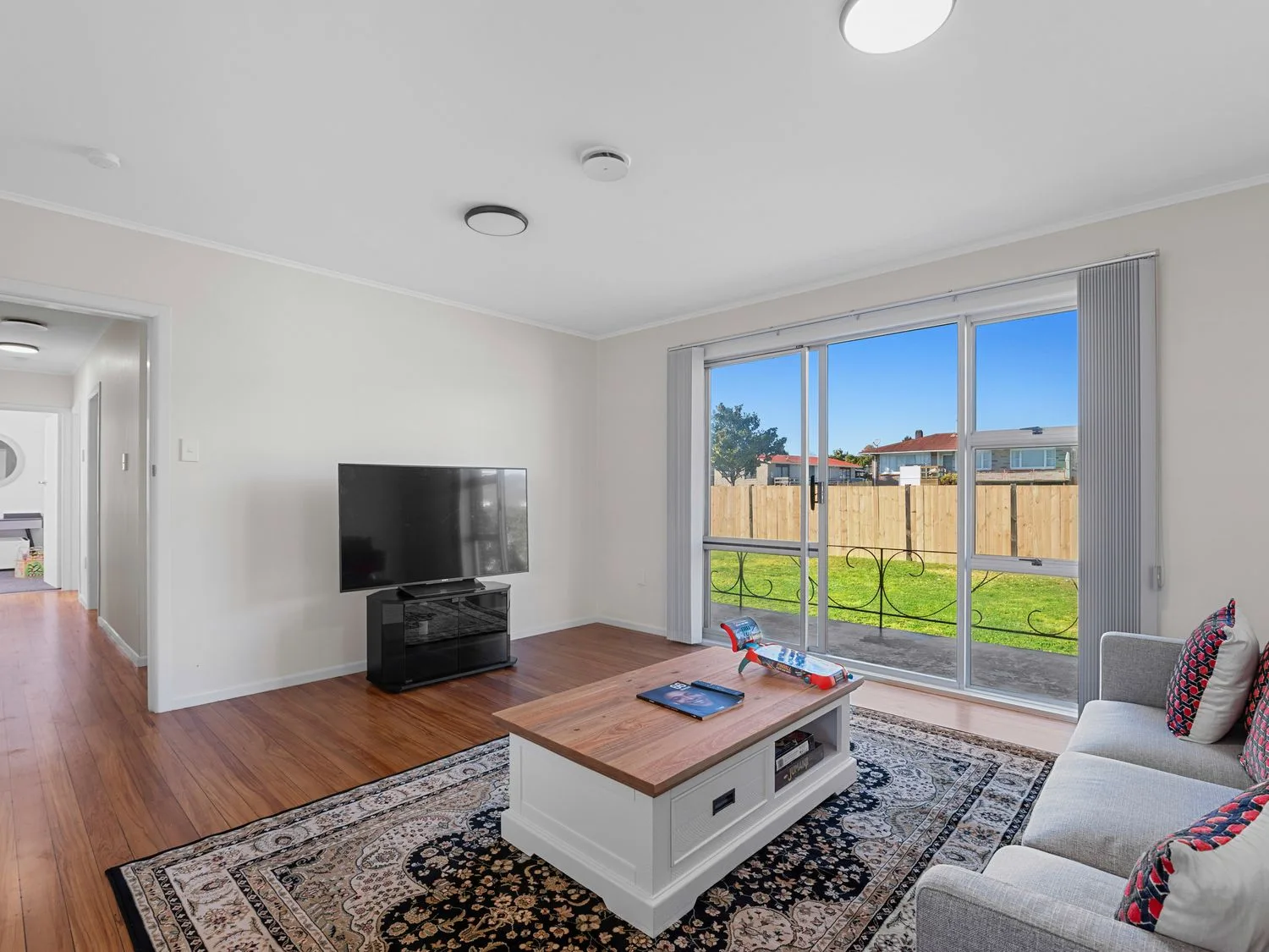 A living room with a sofa and coffee table facing a television on a stand by sliding glass doors at Owhata Retreat - Rotorua Holiday Home in Rotorua