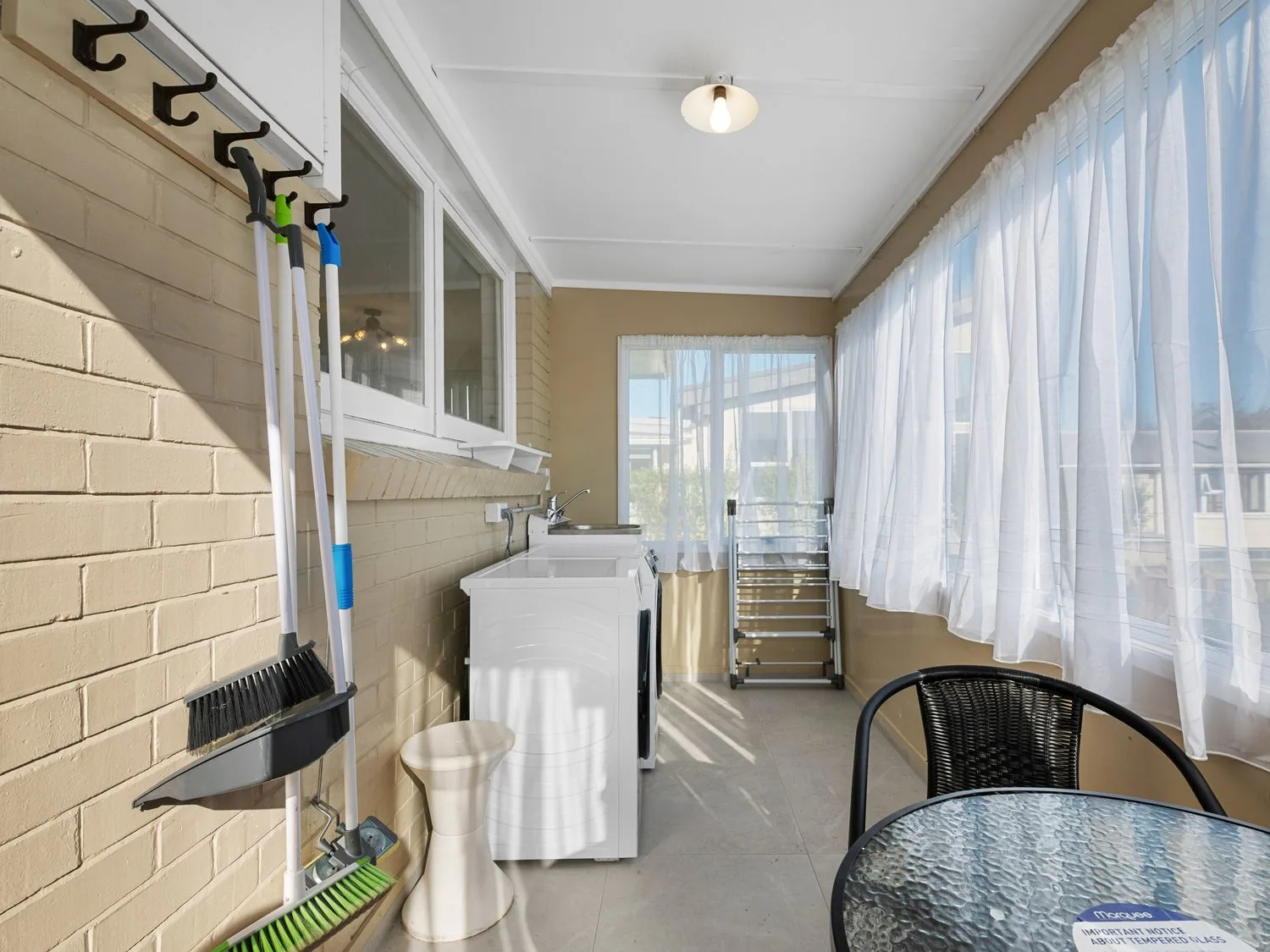 A laundry area with a washing machine, utility sink, and cleaning tools hanging on the wall.