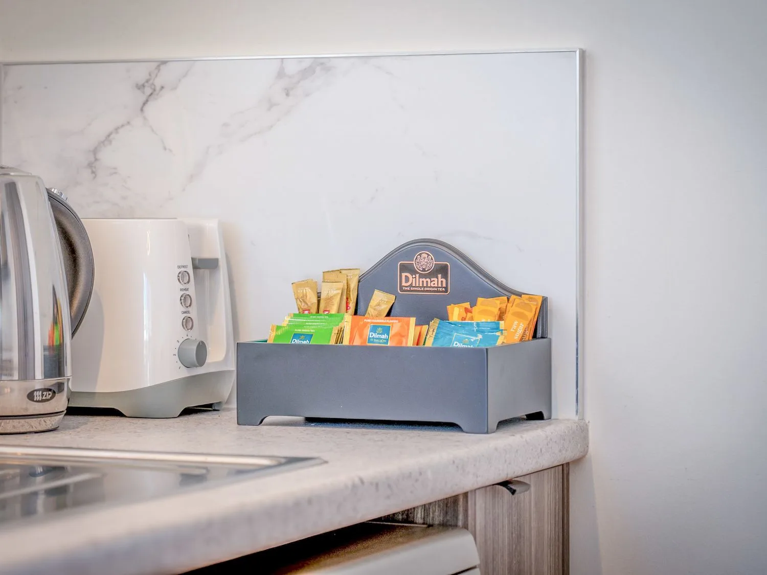 Kitchen counter with a kettle, toaster, and tea packets in a tray.