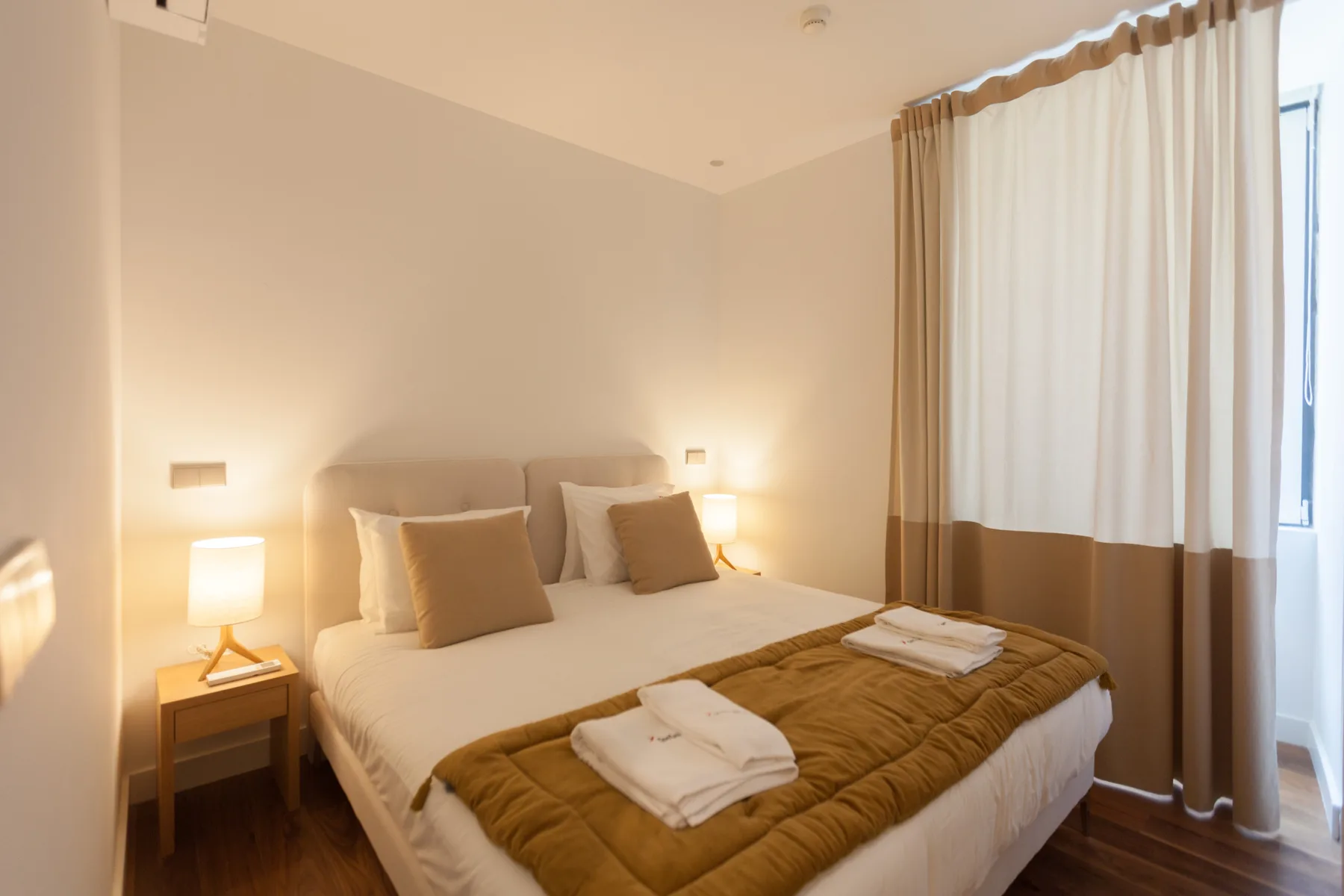 A bedroom with a neatly made bed and curtains beside the window.