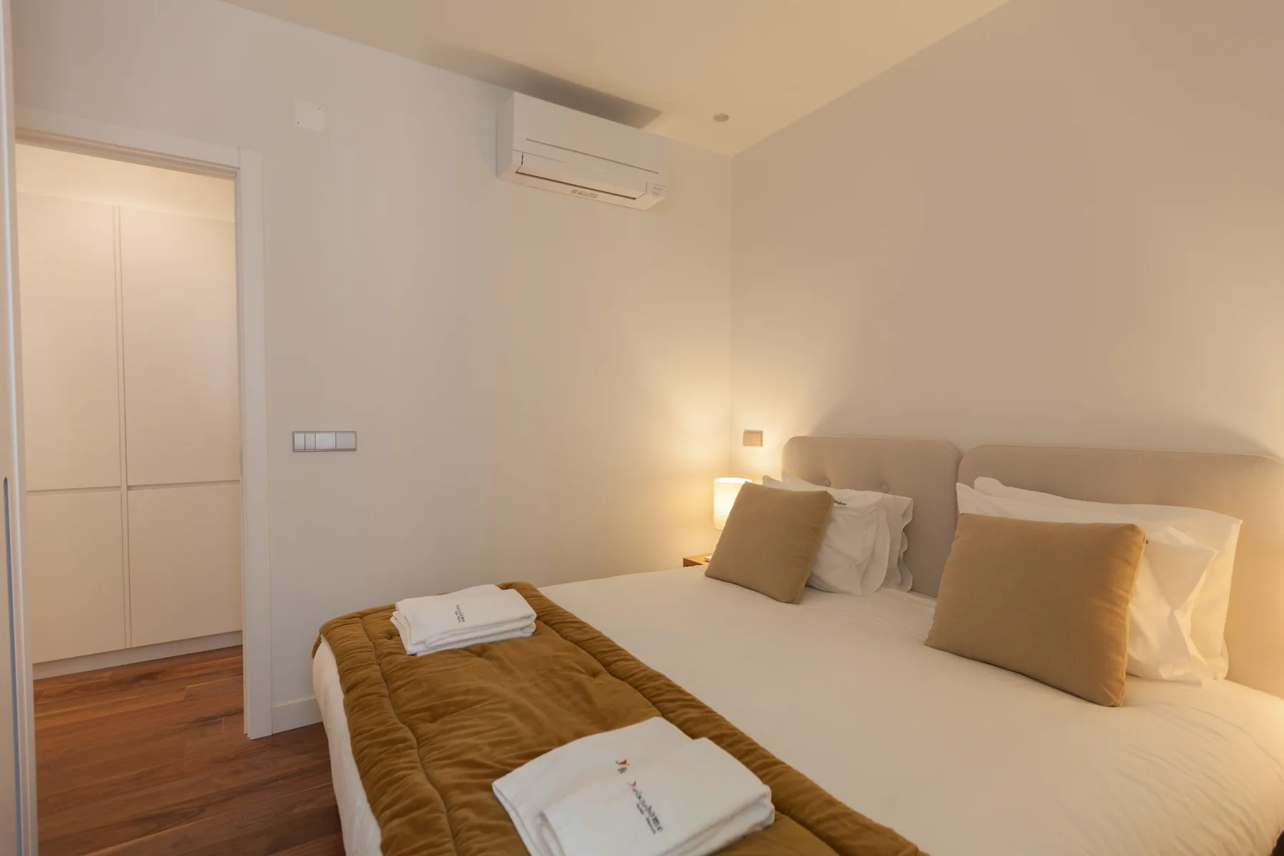 A bedroom with two beds, neutral bedding, and warm bedside lighting.