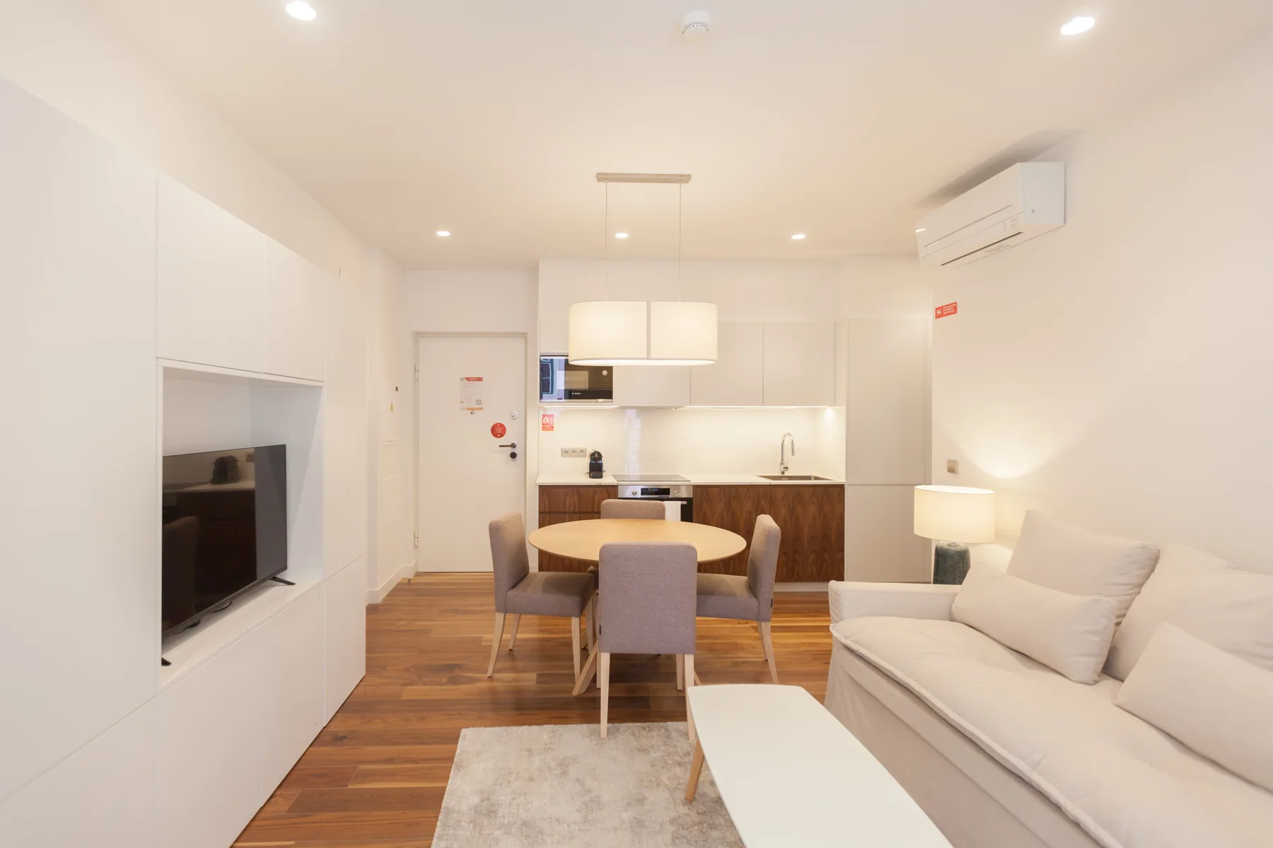 A bright living room with seating, a television, and an open kitchen.