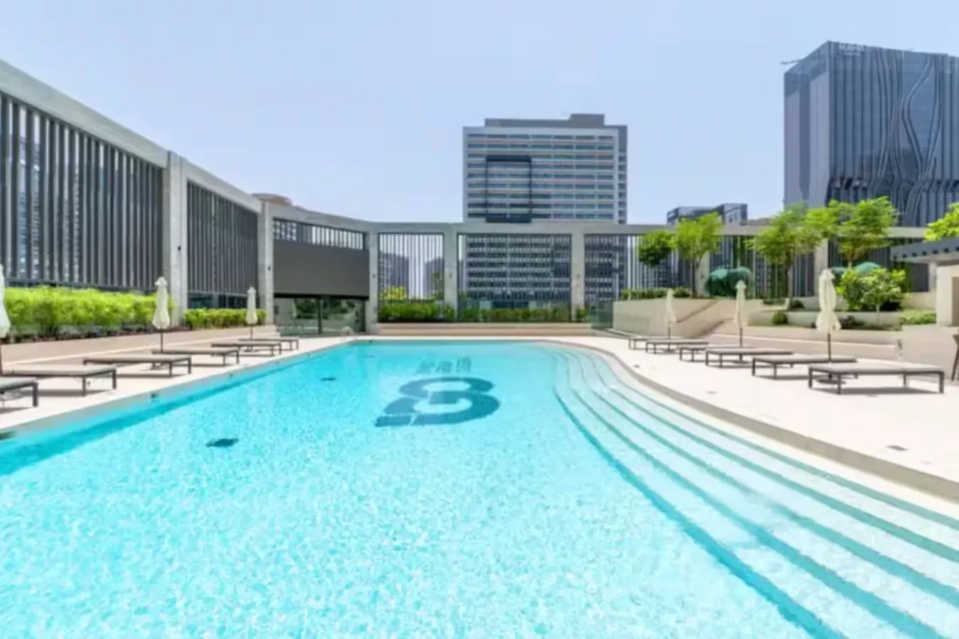 An outdoor swimming pool with lounge seating and modern buildings in the background.