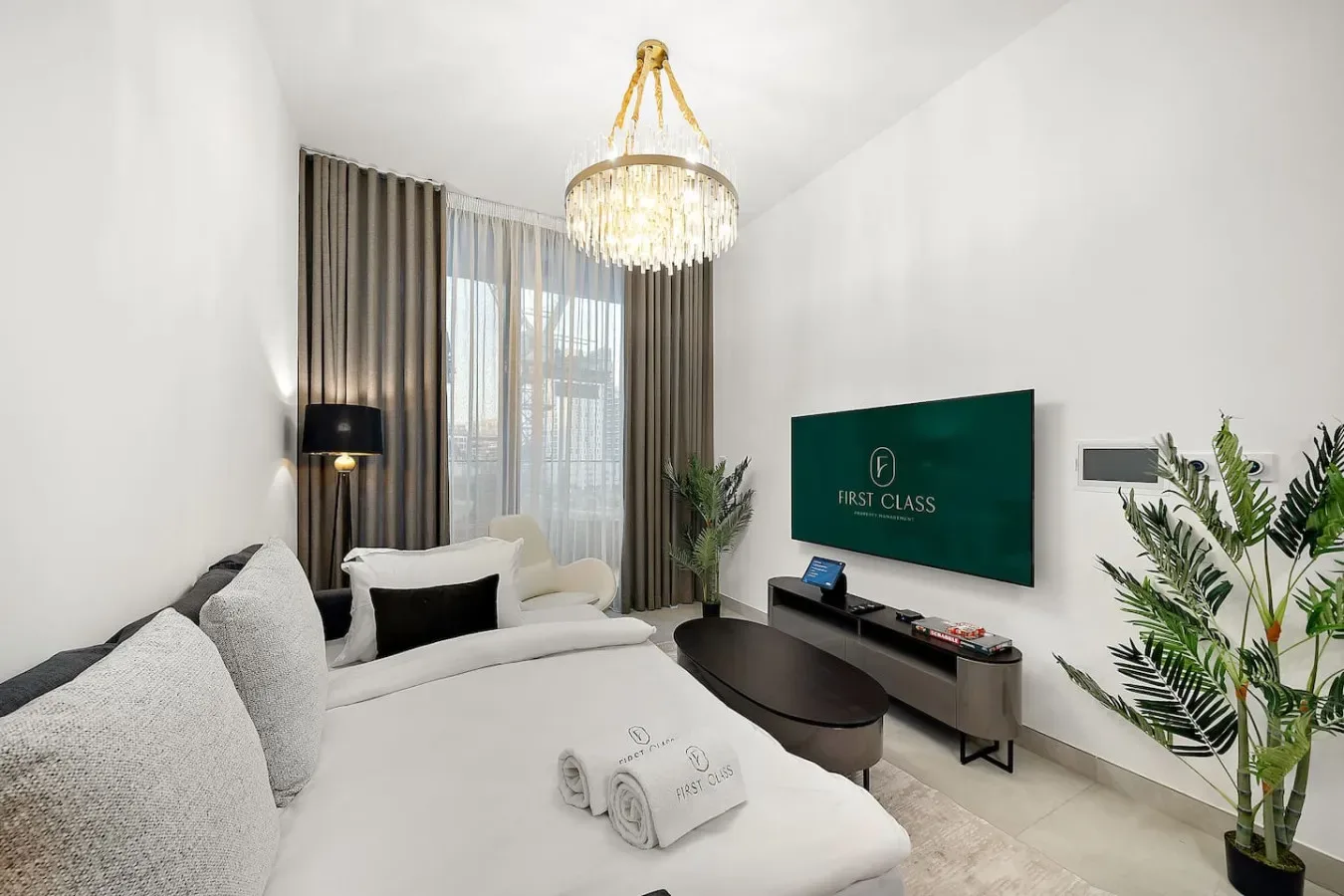 Un dormitorio luminoso con una cama grande, cortinas oscuras y un televisor en la pared.