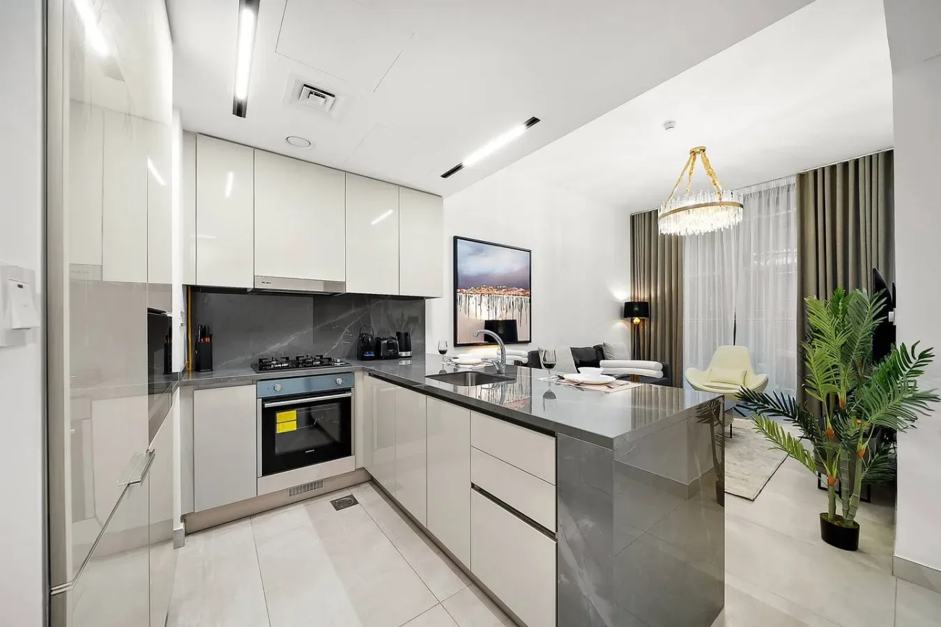 A modern kitchen opens onto a dining area, with a counter and pendant light.