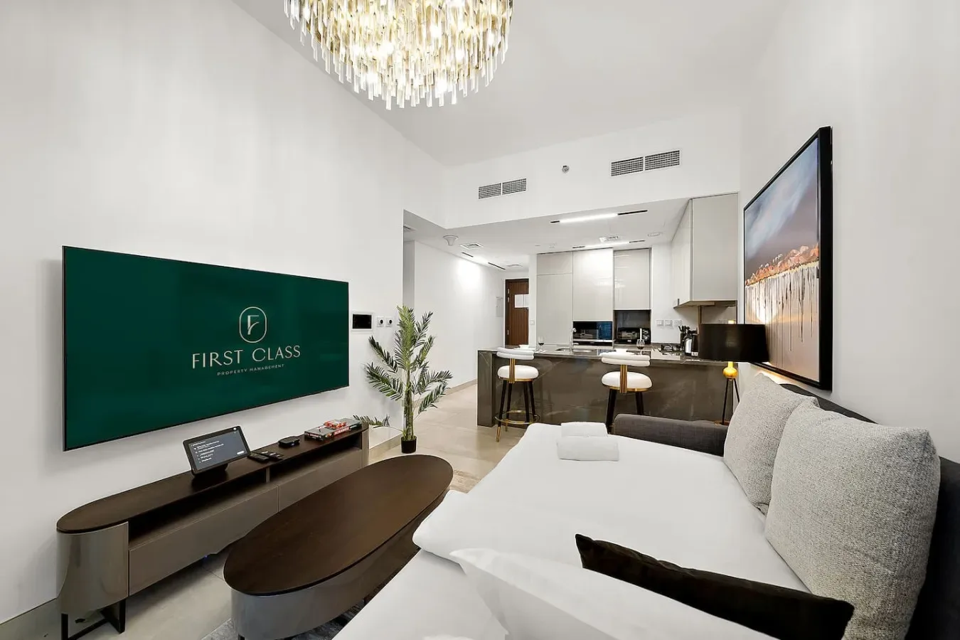 Una sala luminosa con una cama blanca, una pantalla en la pared y una cocina abierta.