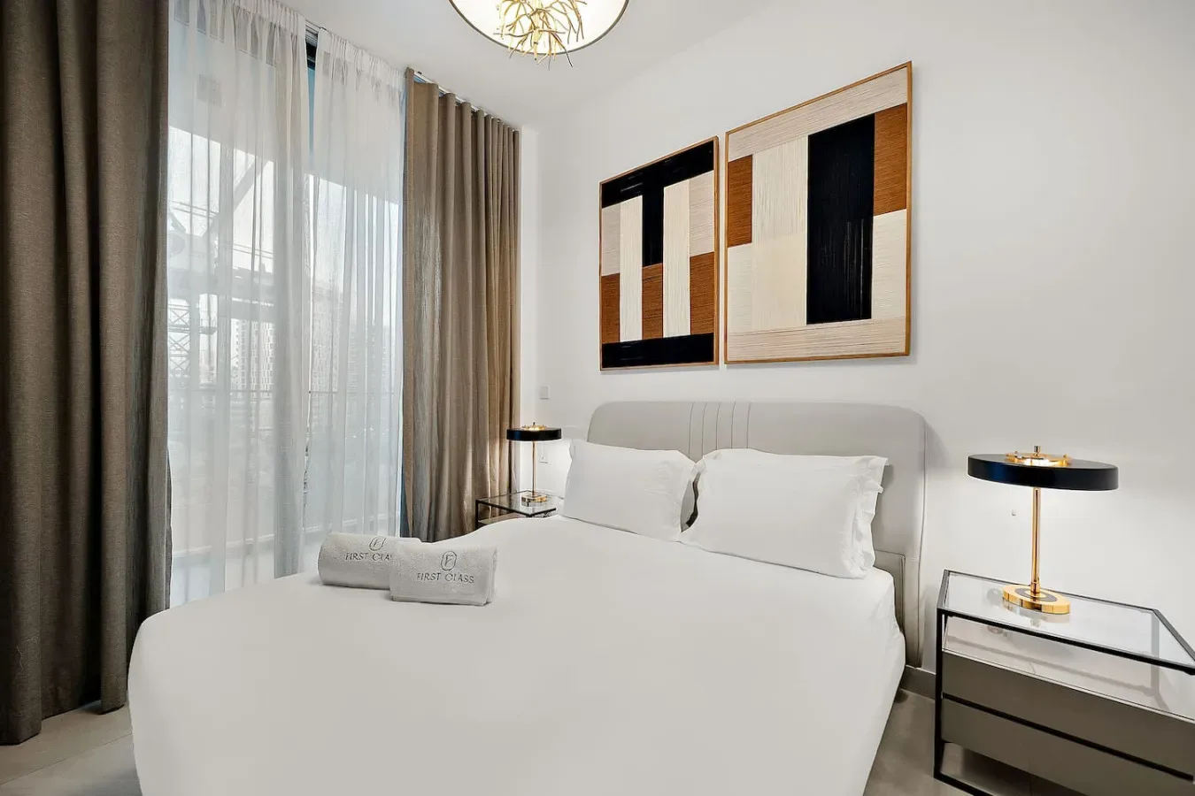 Un dormitorio luminoso con una cama bien tendida, cortinas translúcidas y arte abstracto en la pared.