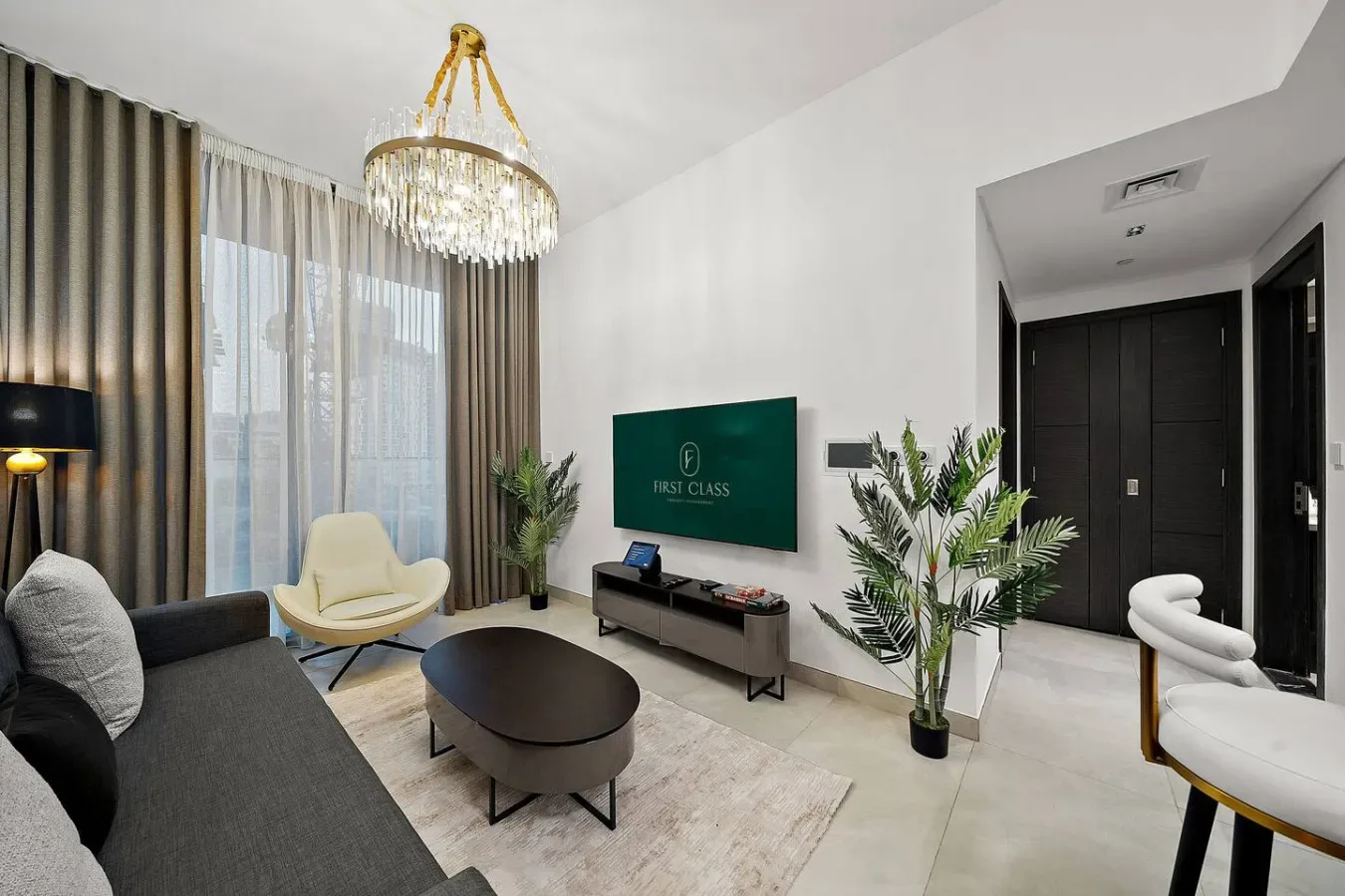 A modern living room with seating, a television, and tall curtained windows.