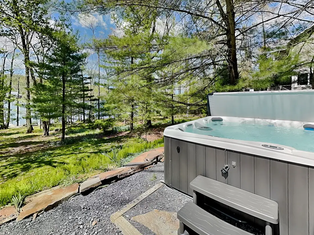 An outdoor hot tub sits beside a wooded area.