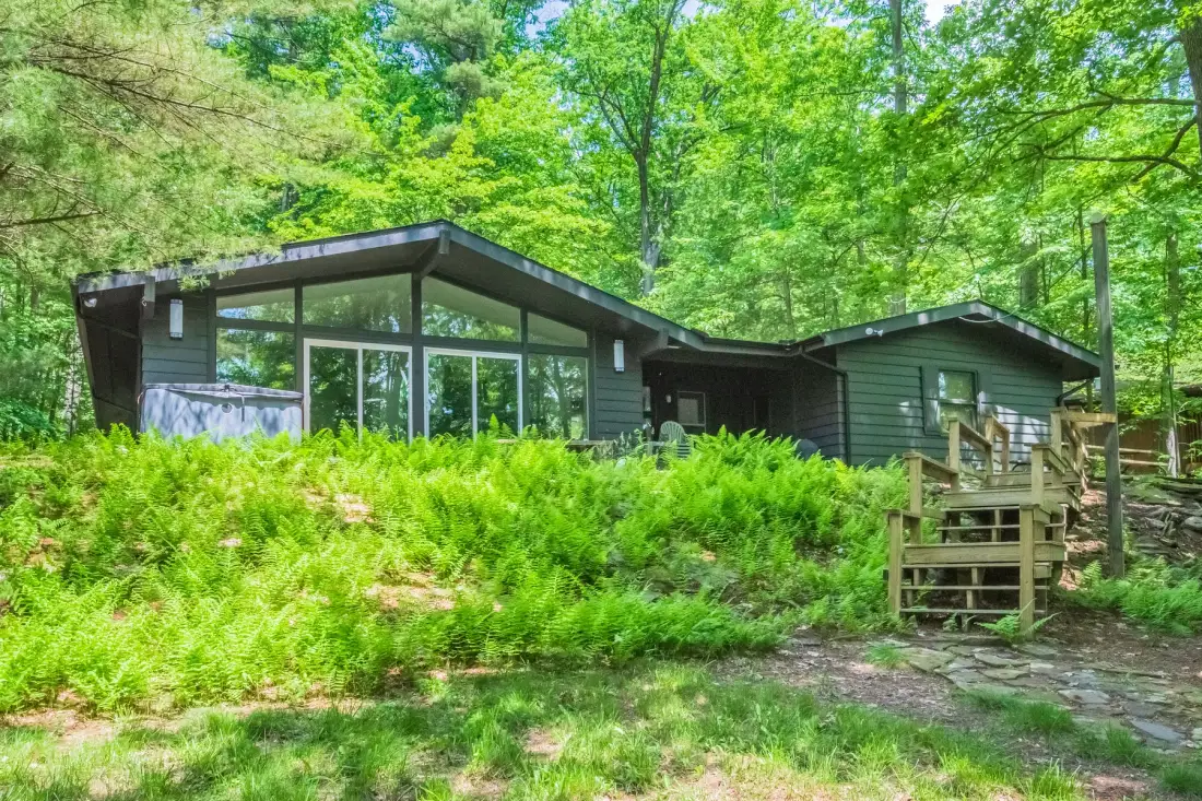 A dark-sided house with a broad glass front sits among trees and lush greenery.