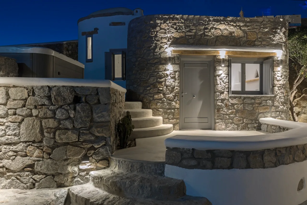 A stone house exterior at night, with illuminated walls and curved steps.