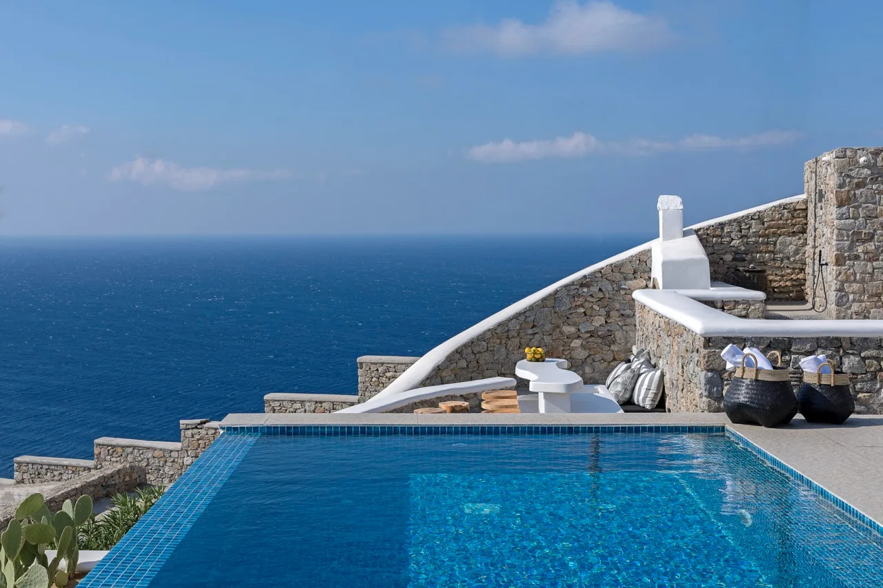 A swimming pool overlooks the sea beside stone terraces.