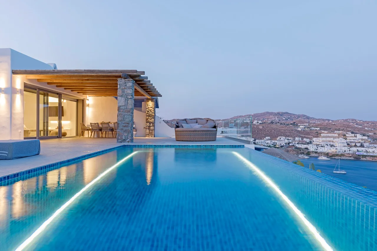 An outdoor swimming pool beside a modern house, overlooking a coastal town.