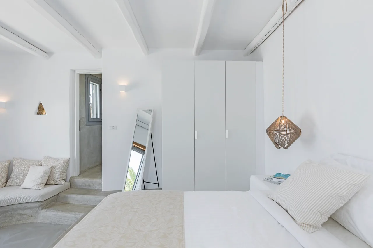A bright bedroom with a large bed, a small sofa, and a standing mirror.