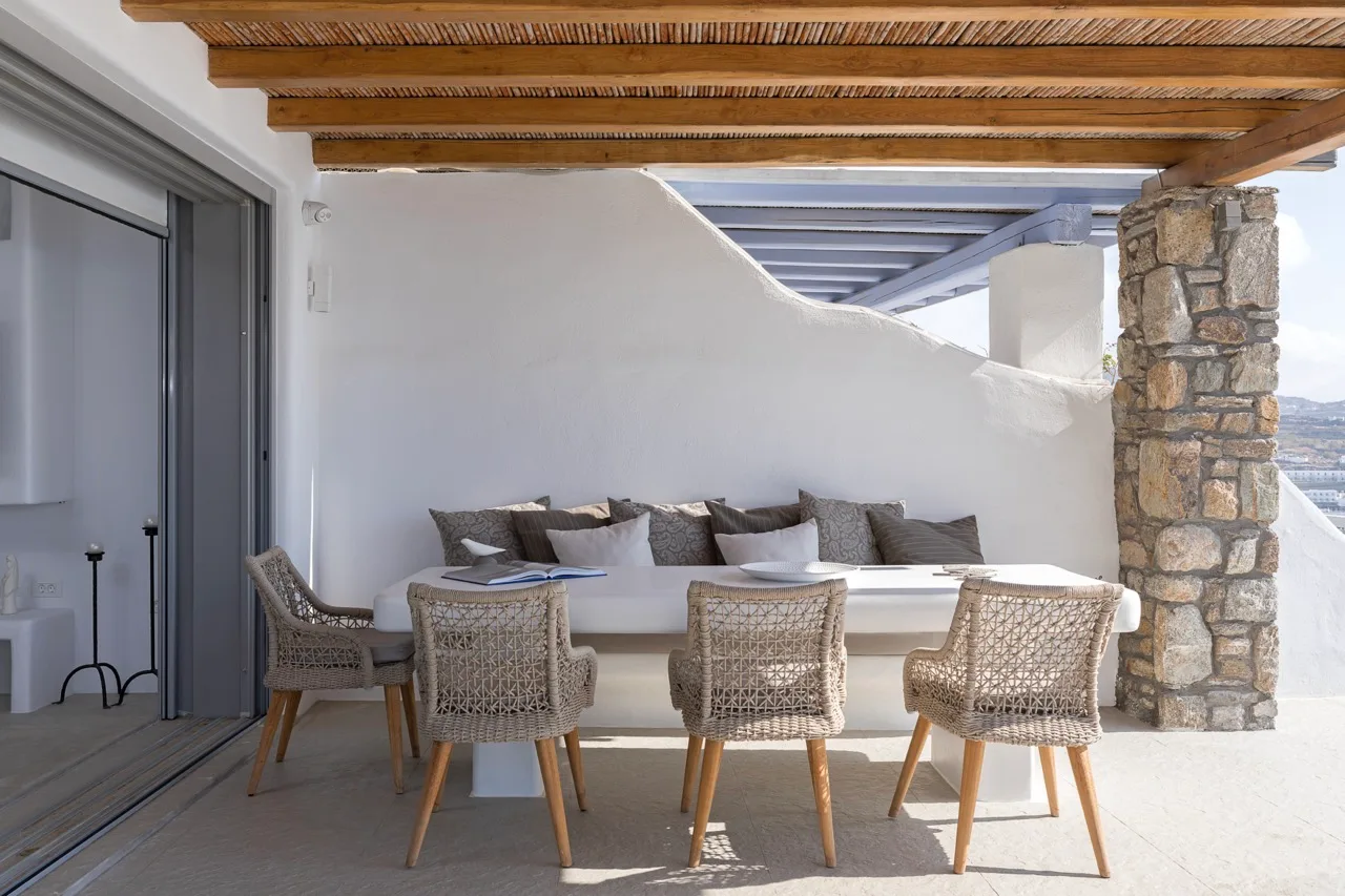 A covered outdoor dining area with a table and woven seating.