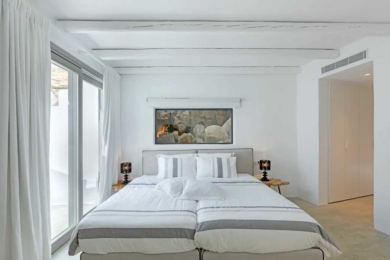 A bright bedroom with a neatly made bed and large windows.