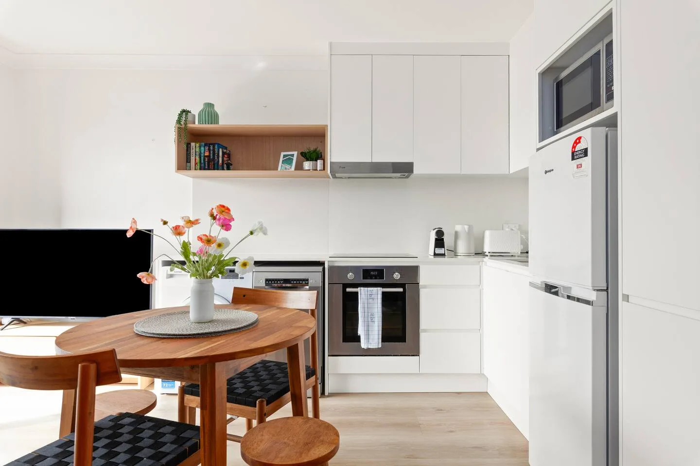 A bright kitchen with white cabinets and a wooden dining table.