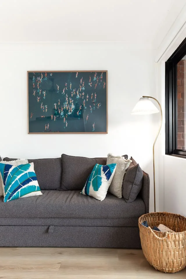 A living room seating area with a dark sofa, colorful cushions, and framed artwork.